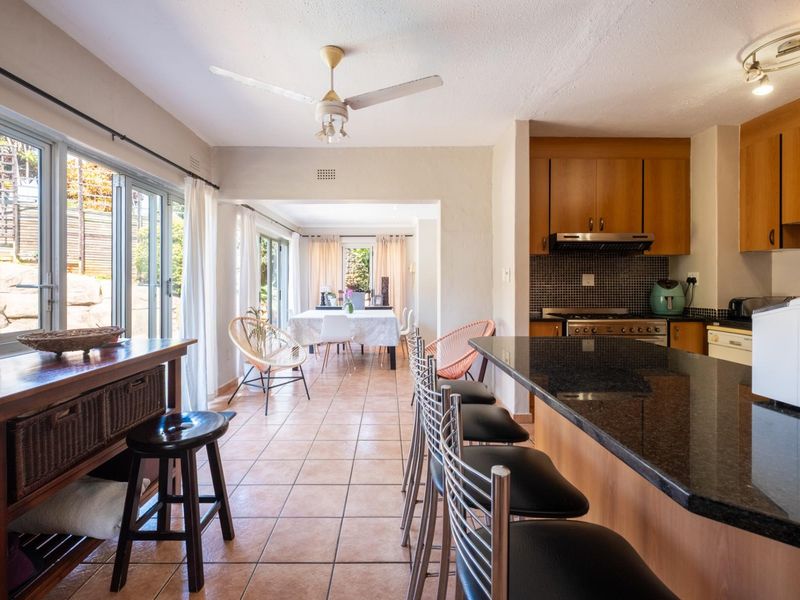 Open-plan kitchen and dining area featuring granite countertops, wooden cabinetry, tiled flooring, and large sliding doors providing access to the outdoor space.