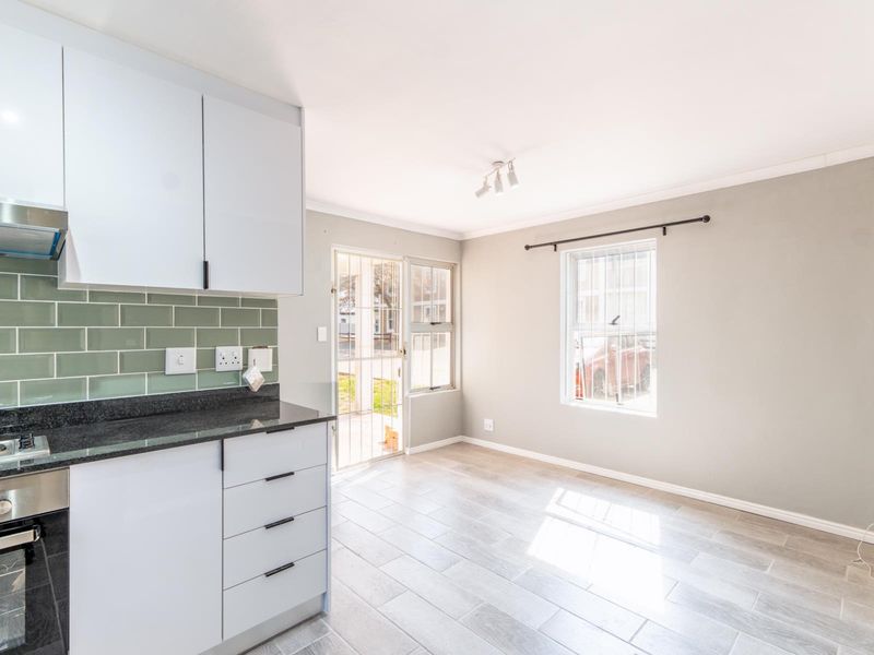 Modern open-plan kitchen and living area featuring sleek white cabinetry, granite countertops, subway tile backsplash, and light-toned tiled flooring with direct outdoor access.