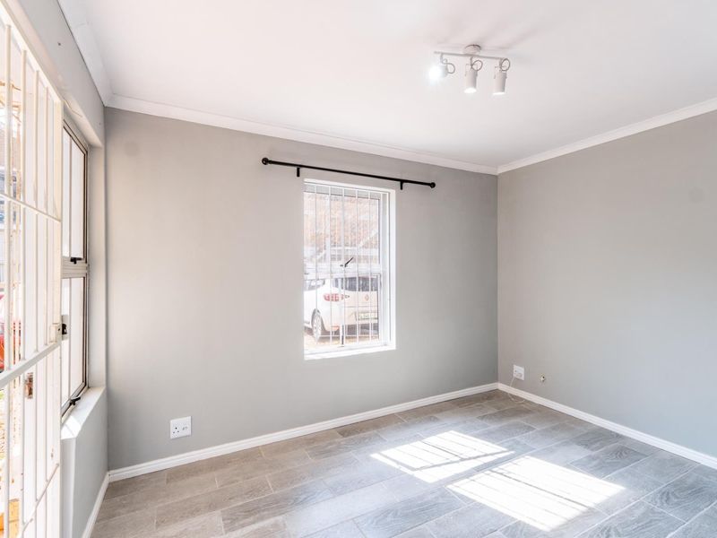 A bright, empty bedroom featuring neutral grey walls, tiled flooring, and security bars on the windows.