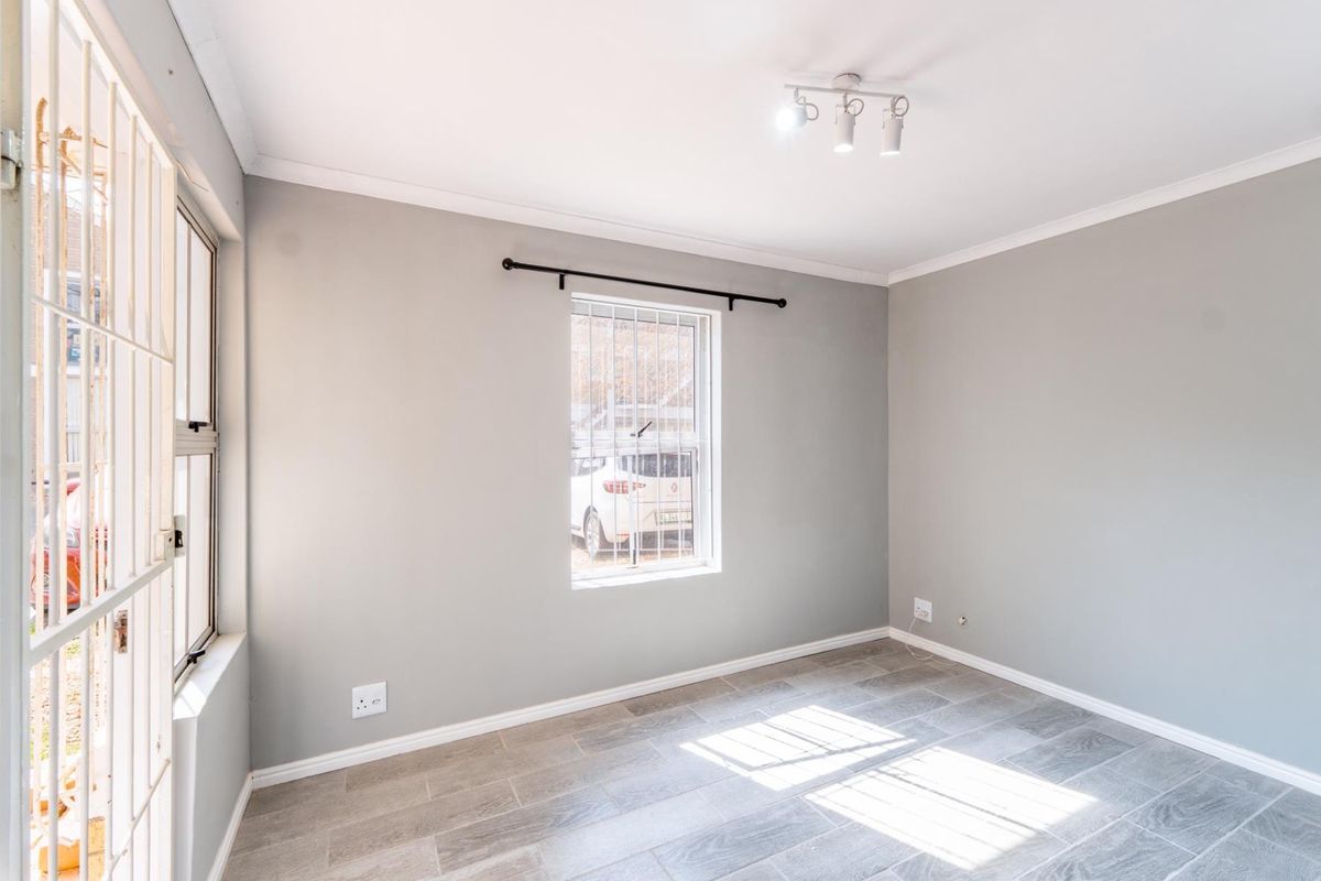 A bright, empty bedroom featuring neutral grey walls, tiled flooring, and security bars on the windows.