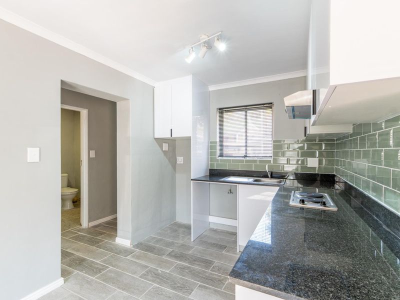 Modern kitchen featuring granite countertops, subway tile backsplash, built-in hob, extractor fan, and ample cabinetry, with an adjacent bathroom visible.