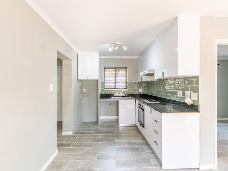A modern, clean kitchen featuring white cabinetry, granite countertops, a green subway tile backsplash, and built-in appliances, presented in an empty, well-maintained state.