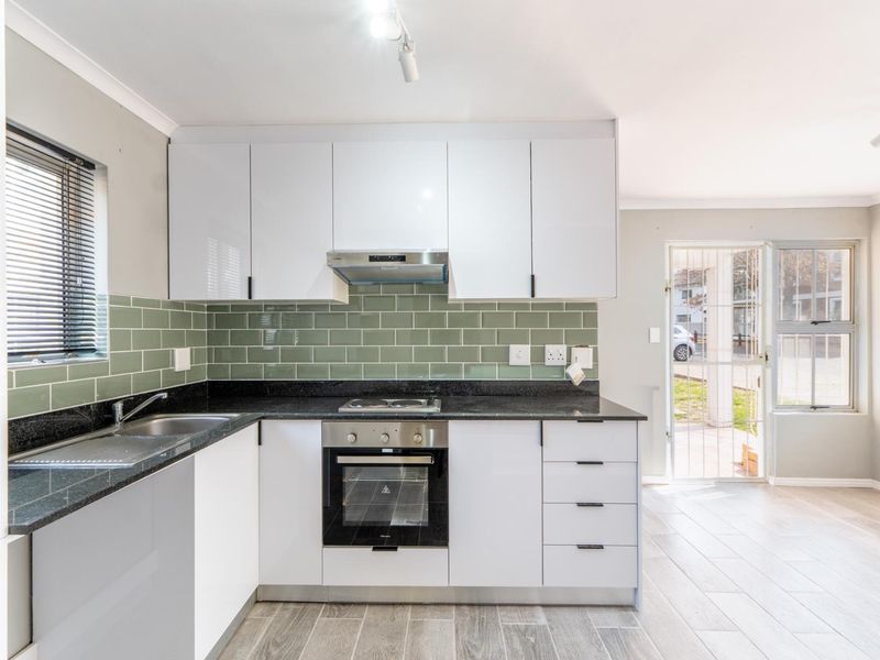 Modern kitchen featuring white cabinetry, granite countertops, green subway tile backsplash, built-in oven, and hob, with direct access to the exterior.