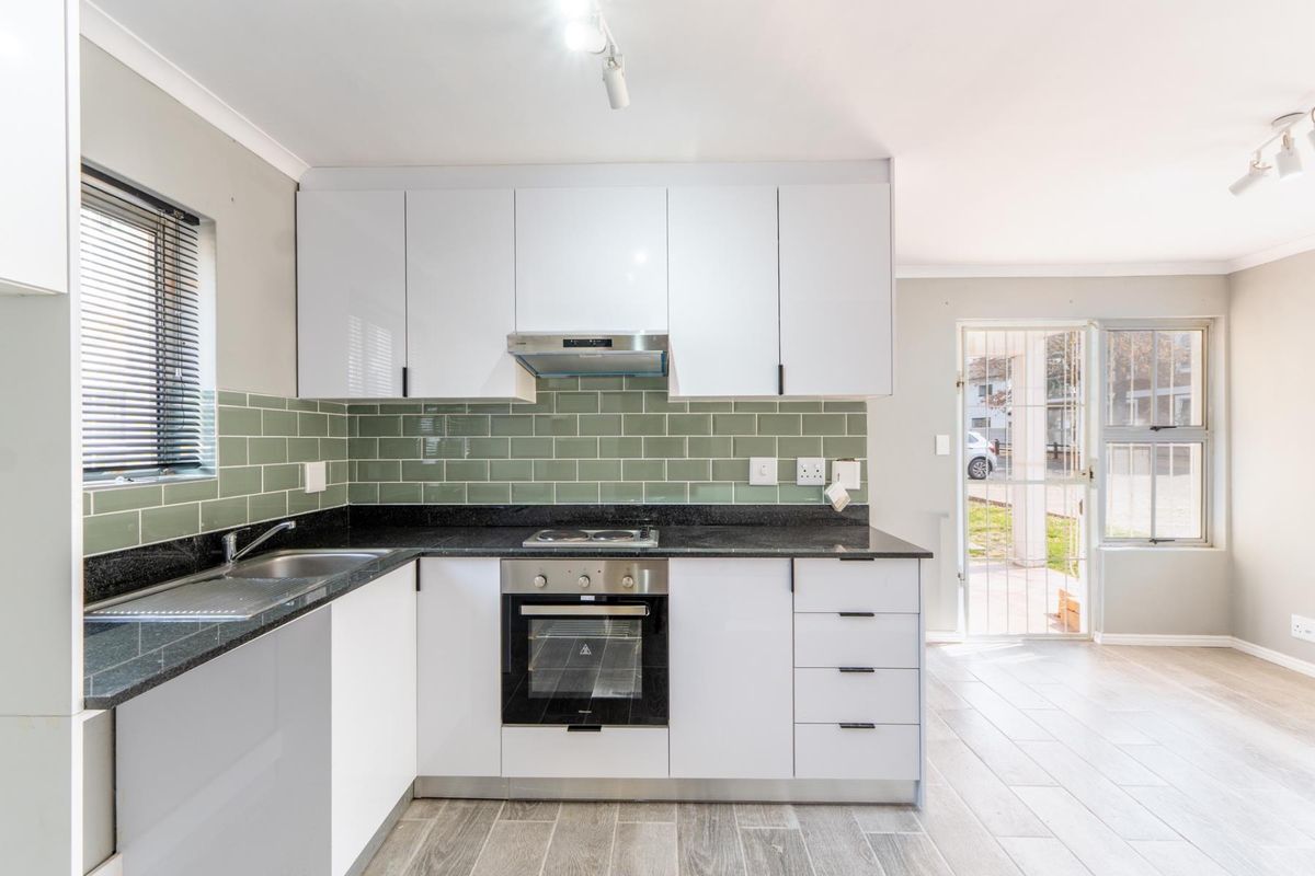 Modern kitchen featuring white cabinetry, granite countertops, green subway tile backsplash, built-in oven, and hob, with direct access to the exterior.