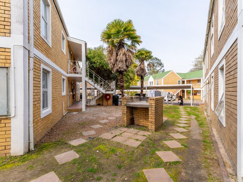 Rear exterior view of the apartment complex featuring a communal brick braai area, paved pathways, and external staircases leading to upper units.