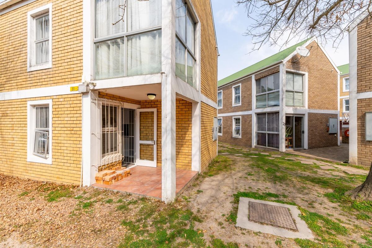 Exterior view of a multi-story apartment complex featuring brick facades, tiled ground-floor patios, and shared garden space.