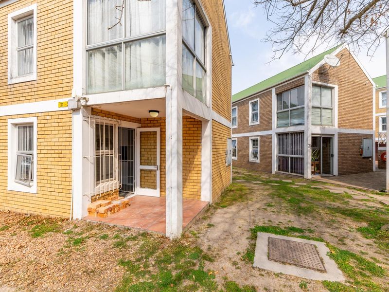 Exterior view of a multi-story apartment complex featuring brick facades, tiled ground-floor patios, and shared garden space.