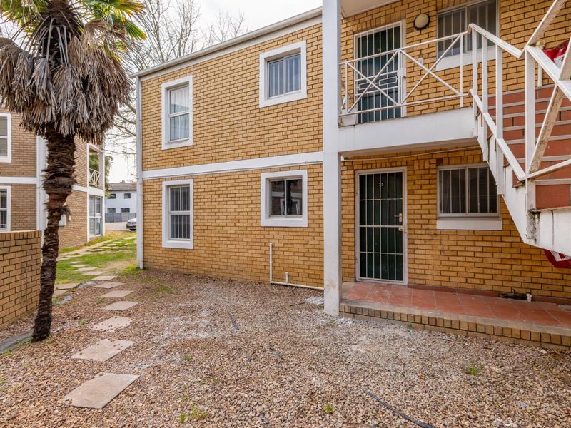 Exterior view of a face brick apartment building featuring an external staircase, security gates, and a paved ground level area.