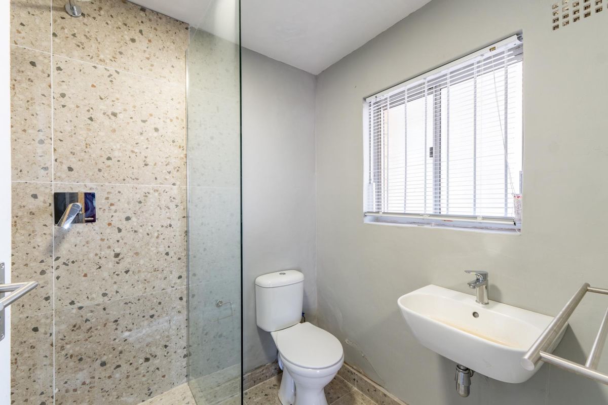 A clean, modern bathroom featuring a glass-enclosed shower with terrazzo-style tiling, a wall-mounted basin, and a heated towel rail.