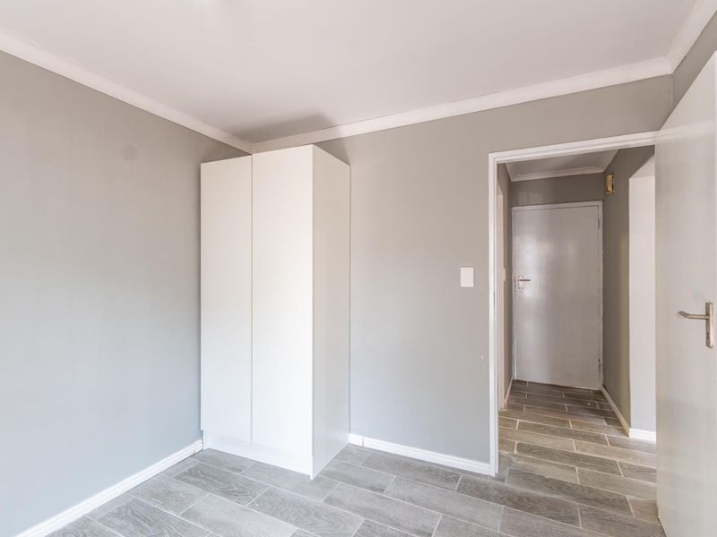 A clean, empty bedroom featuring neutral grey walls, tiled flooring, and a built-in wardrobe, offering a versatile space ready for personalization.
