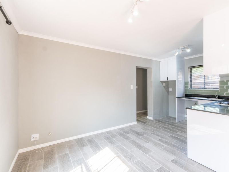 An open-plan living and kitchen area featuring modern grey tiled flooring, neutral wall tones, and a functional kitchen space with built-in cabinetry.
