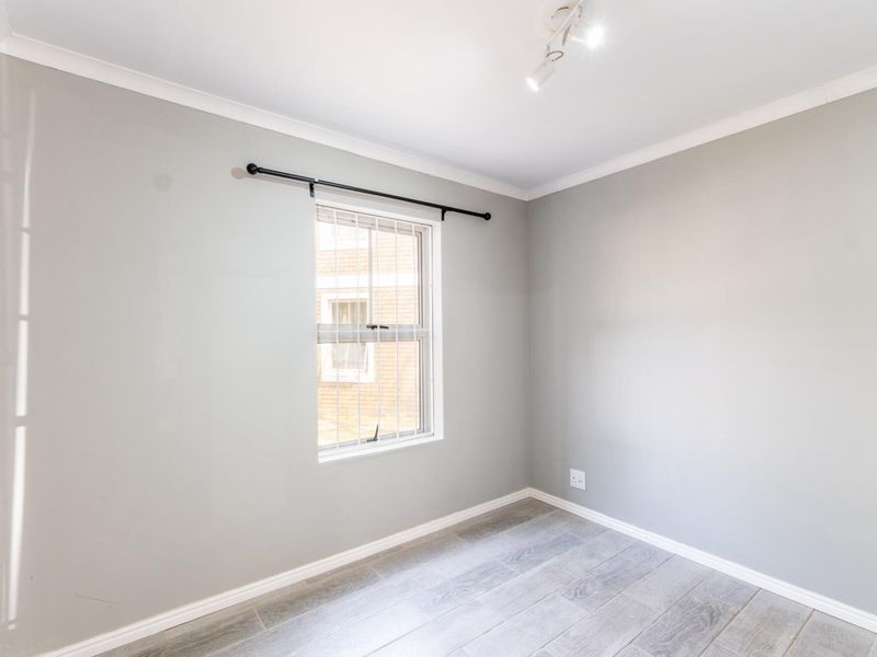 A clean, empty bedroom featuring neutral grey walls, tiled flooring, and a window fitted with security bars.