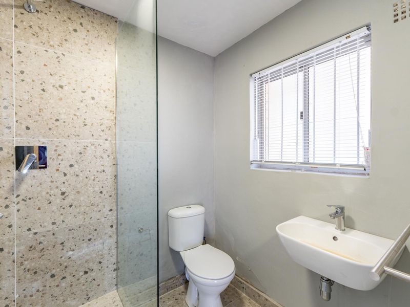 A clean, modern bathroom featuring a glass-enclosed shower with terrazzo-style tiling, a wall-mounted basin, and a heated towel rail.