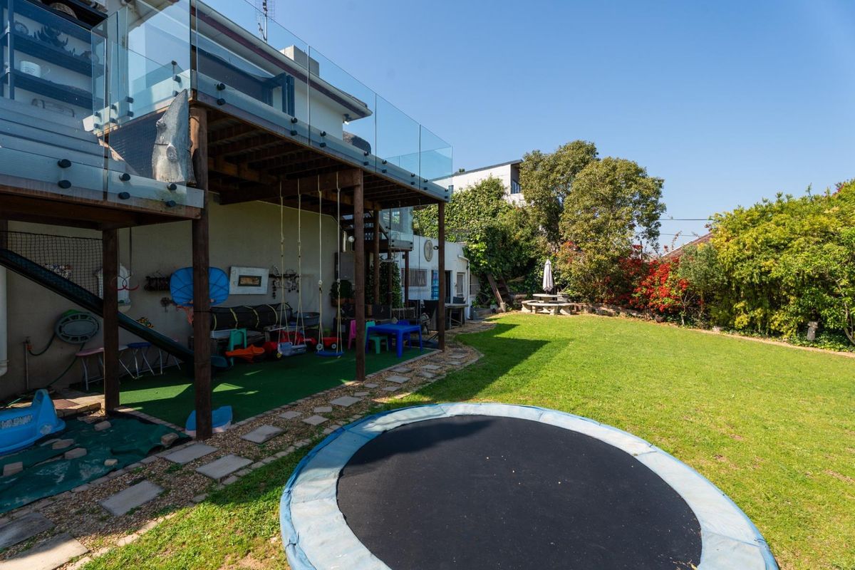 Rear garden featuring a spacious lawn, stone pathway, and a raised deck with a modern glass balustrade and spiral staircase access.