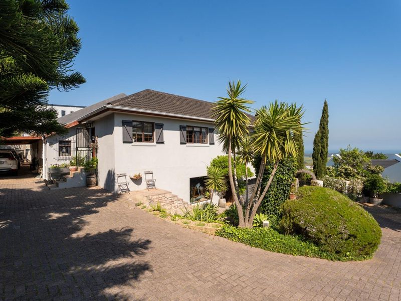 Front exterior view of a residential house featuring a paved driveway, landscaped garden, and tiled roof with shutters.