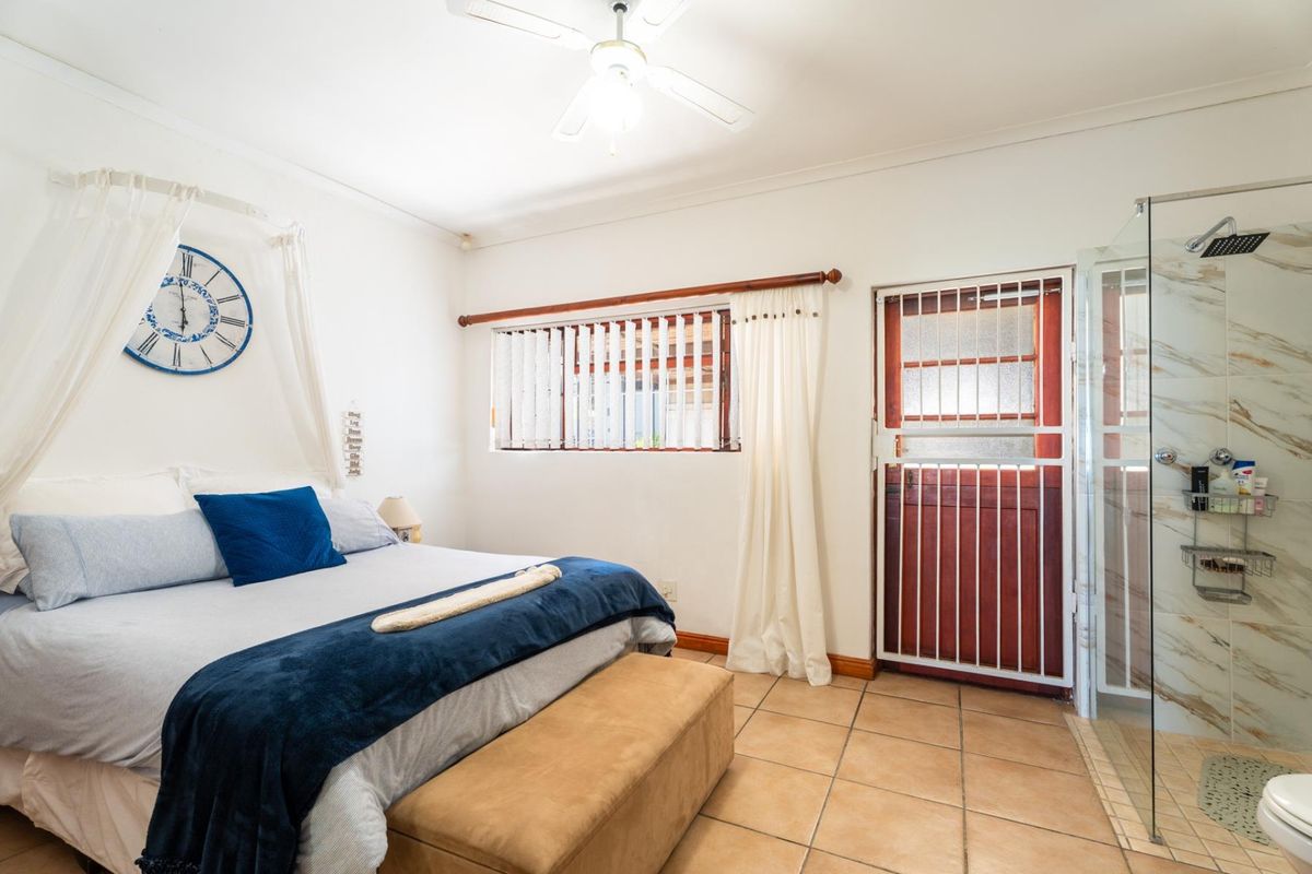 A bedroom featuring tiled flooring, a ceiling fan, and an en-suite shower with a glass enclosure and security gate access.