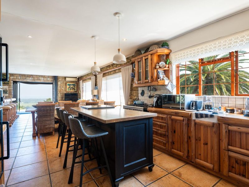 Spacious open-plan kitchen and living area featuring rustic wooden cabinetry, a central island, stone feature walls, and large windows with garden views.