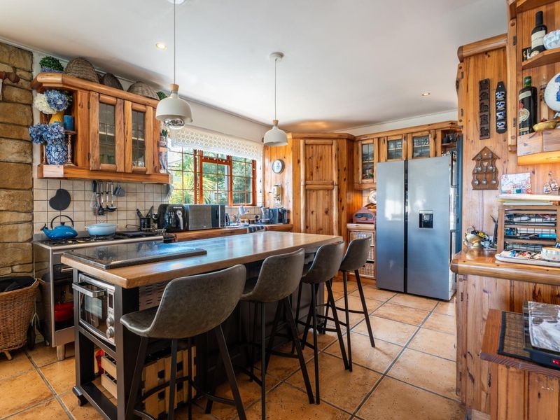 A rustic-style kitchen featuring extensive timber cabinetry, a stone feature wall, terracotta floor tiles, and a central island with breakfast bar seating.