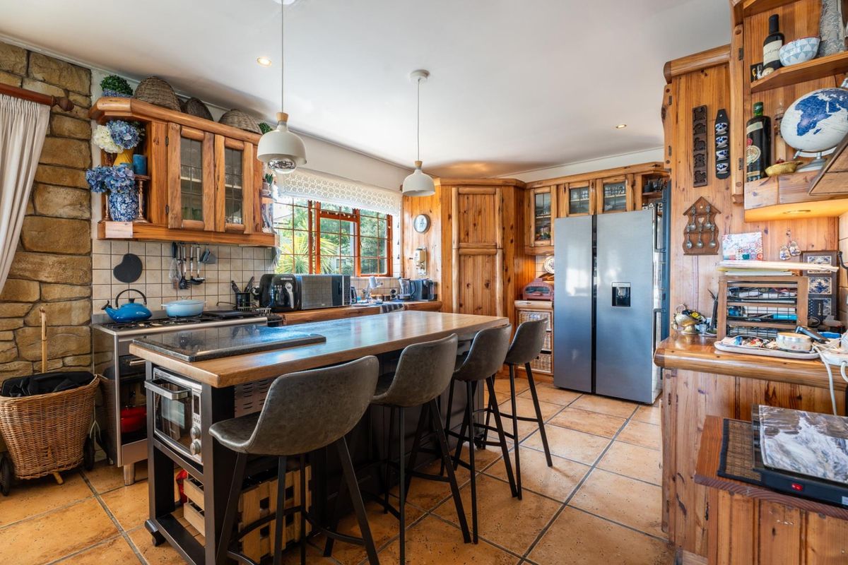 A rustic-style kitchen featuring extensive timber cabinetry, a stone feature wall, terracotta floor tiles, and a central island with breakfast bar seating.