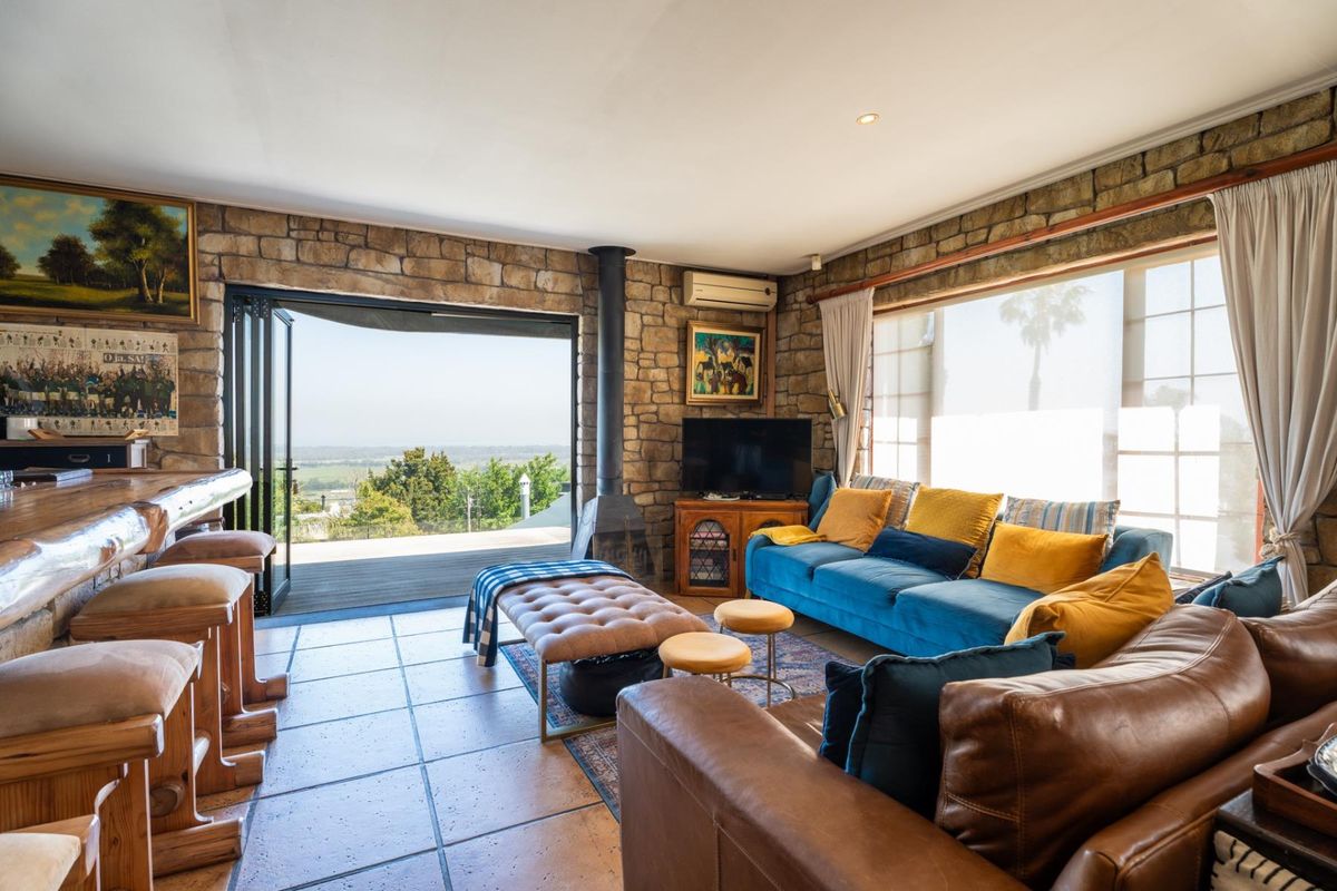 Spacious living room featuring rustic stone walls, tiled flooring, a freestanding fireplace, and large stacking doors opening to an outdoor deck with scenic views.