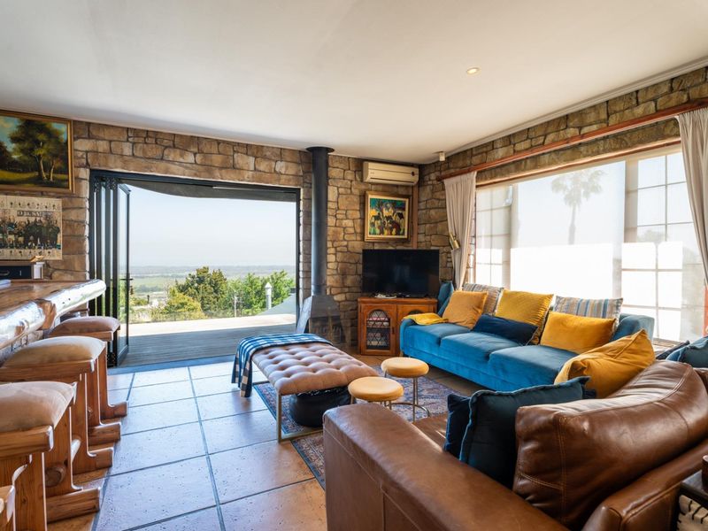 Spacious living room featuring rustic stone walls, tiled flooring, a freestanding fireplace, and large stacking doors opening to an outdoor deck with scenic views.
