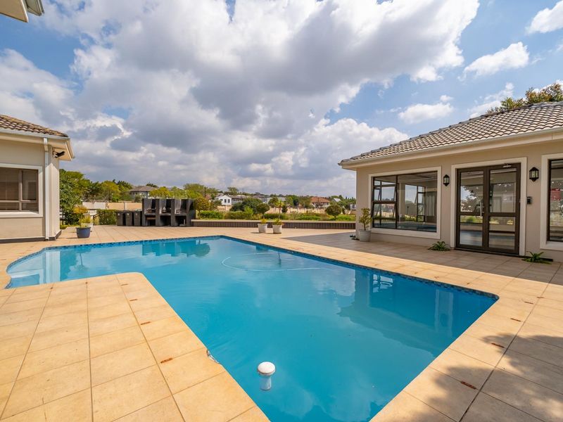 Spacious outdoor pool area featuring a tiled deck, built-in braai, and direct access to the residence through glass sliding doors.