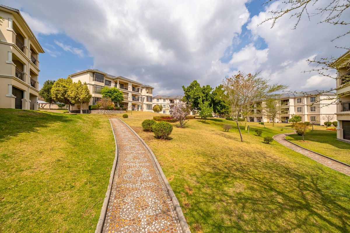 A well-maintained communal garden area featuring paved pathways winding between multi-story apartment buildings in a residential complex.
