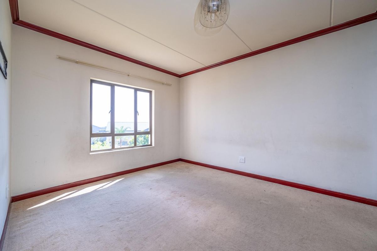 An empty bedroom featuring carpeted flooring, an aluminium window, and decorative red skirting boards, offering a blank canvas for potential renovation.
