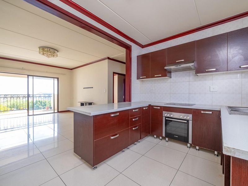 Open-plan kitchen and living area featuring dark wood cabinetry, built-in appliances, tiled flooring, and access to a balcony through sliding glass doors.