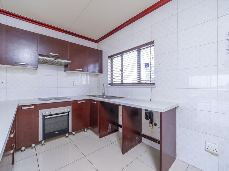 A functional kitchen featuring dark wood cabinetry, built-in oven and hob, tiled finishes, and a dedicated space for an under-counter appliance.
