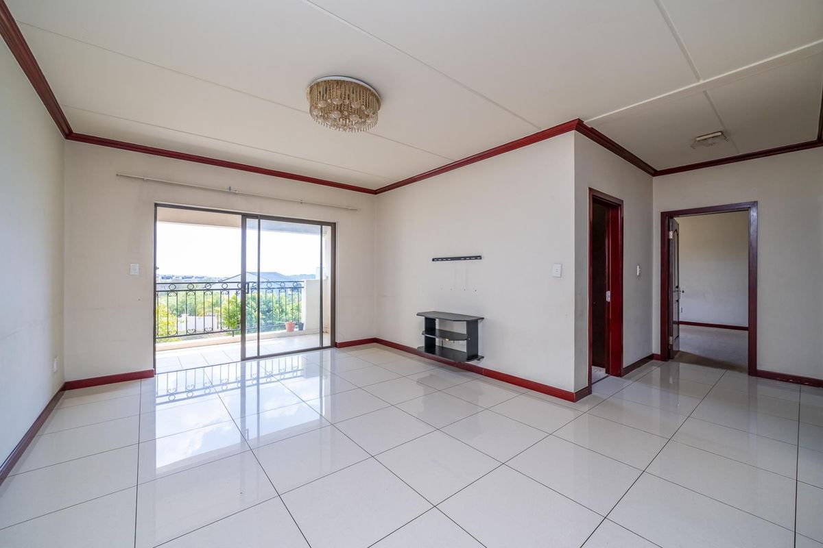 Spacious, light-filled living area featuring neutral tiled flooring, coved ceilings, and direct access to a private balcony through sliding glass doors.