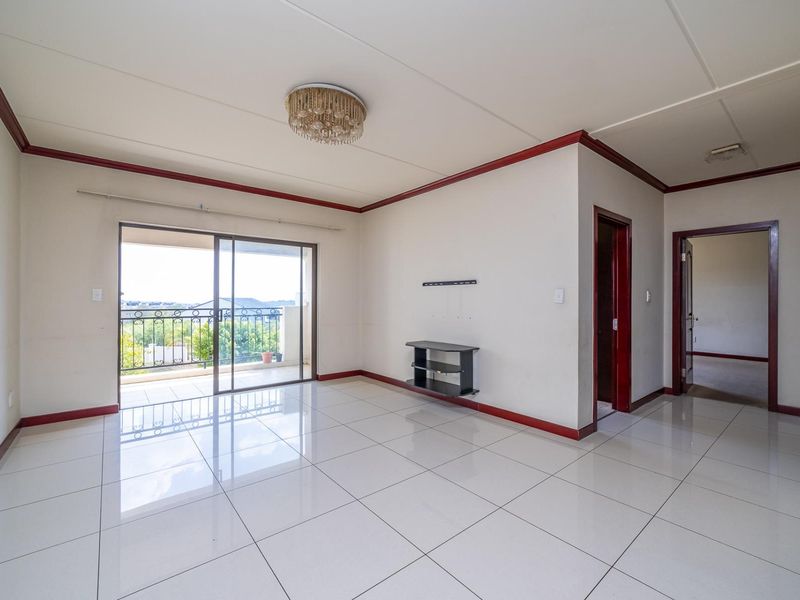 Spacious, light-filled living area featuring neutral tiled flooring, coved ceilings, and direct access to a private balcony through sliding glass doors.