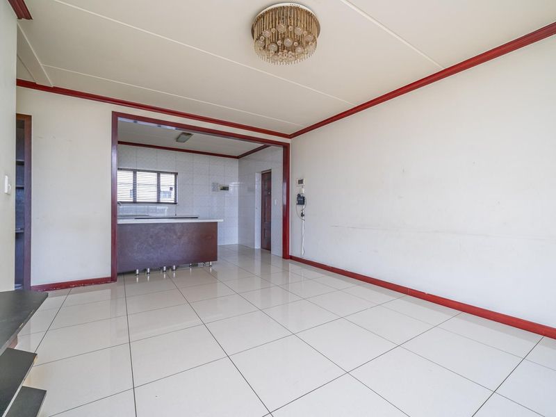 An open-plan living area featuring tiled flooring, a central light fixture, and a connected kitchen space with a breakfast bar.