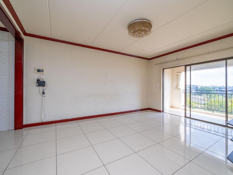 An empty, open-plan living area featuring large floor tiles, decorative coving, and direct access to a balcony through sliding glass doors.