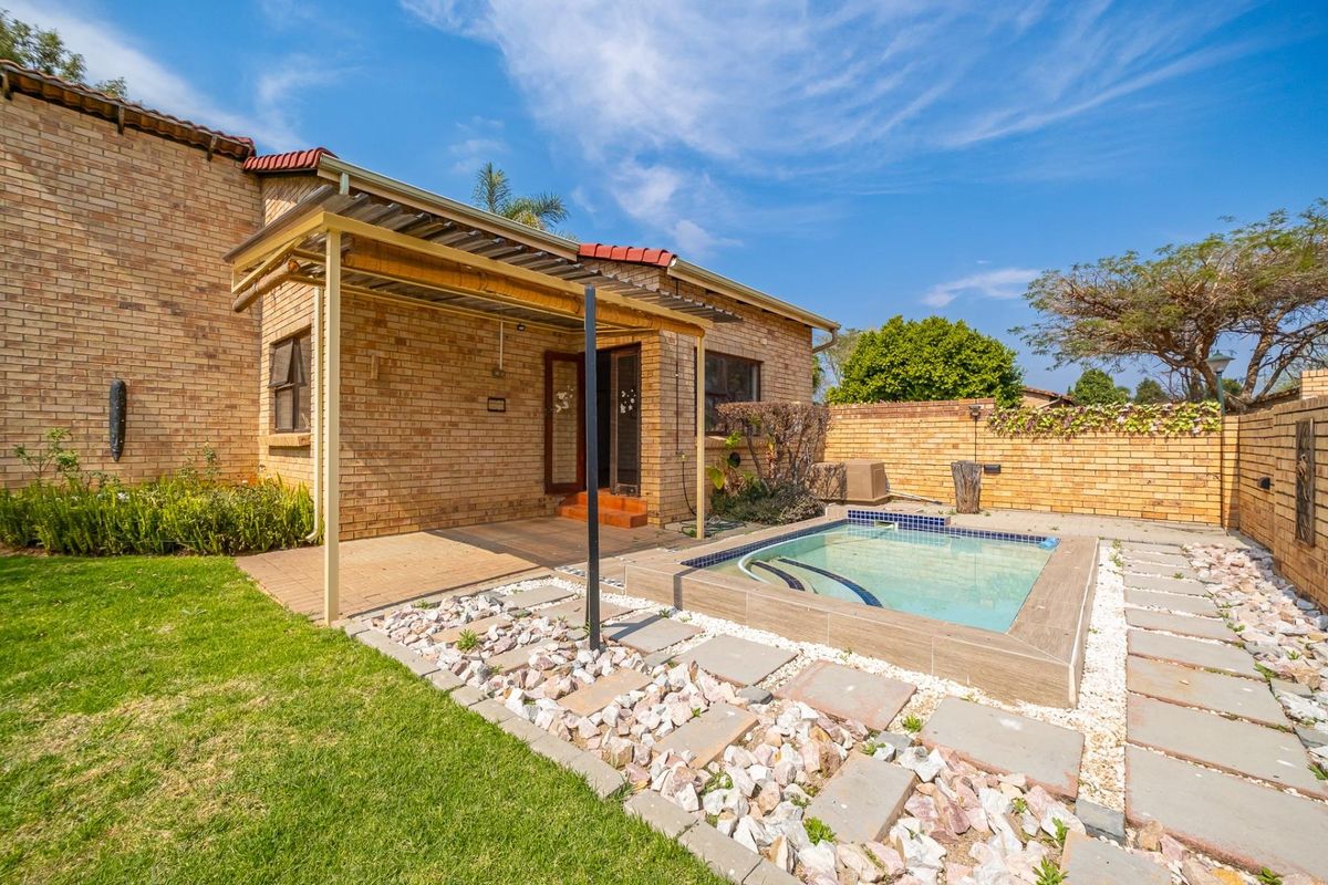 Rear exterior view featuring a brick house, covered patio area, and a small swimming pool set within a landscaped garden with paved pathways.
