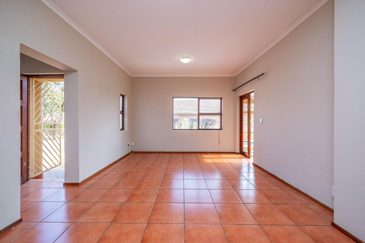 An empty, well-lit living area featuring neutral walls, terracotta-style floor tiles, and direct access to an outdoor space through a sliding glass door.
