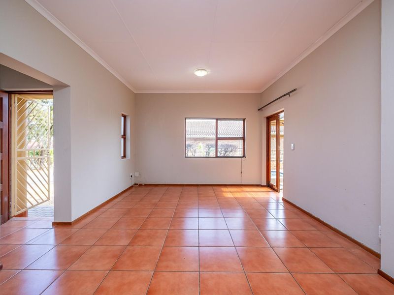 An empty, well-lit living area featuring neutral walls, terracotta-style floor tiles, and direct access to an outdoor space through a sliding glass door.