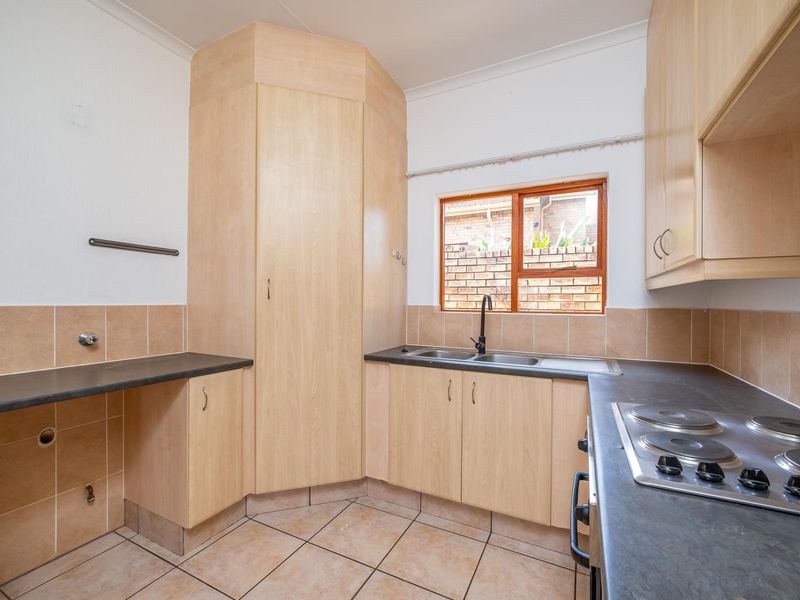 A functional kitchen featuring light wood cabinetry, dark laminate countertops, a built-in electric hob, and tiled splashbacks with a double sink.