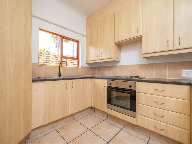 A functional kitchen featuring light wood-look cabinetry, a built-in oven with gas hob, tiled splashbacks, and ceramic floor tiles.