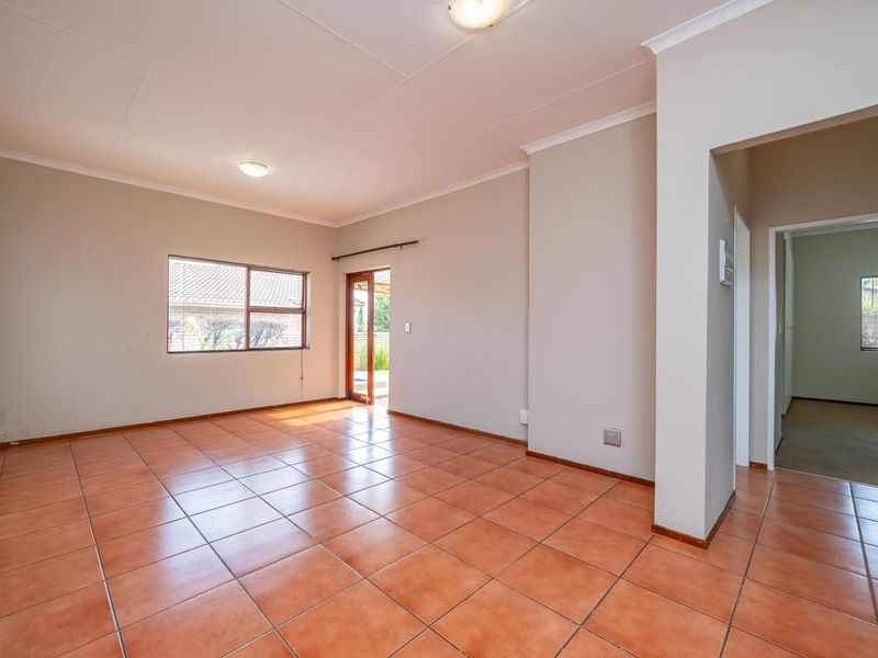 A spacious, empty living room featuring neutral walls, ceramic tile flooring, and natural light through a large window and sliding glass door.