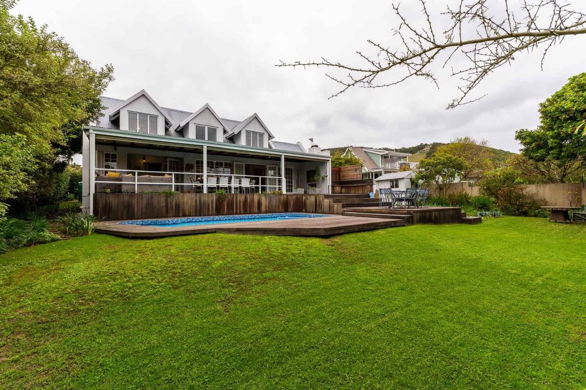 Rear view of the property featuring a swimming pool, extensive timber decking, a covered patio area, and a well-maintained garden.