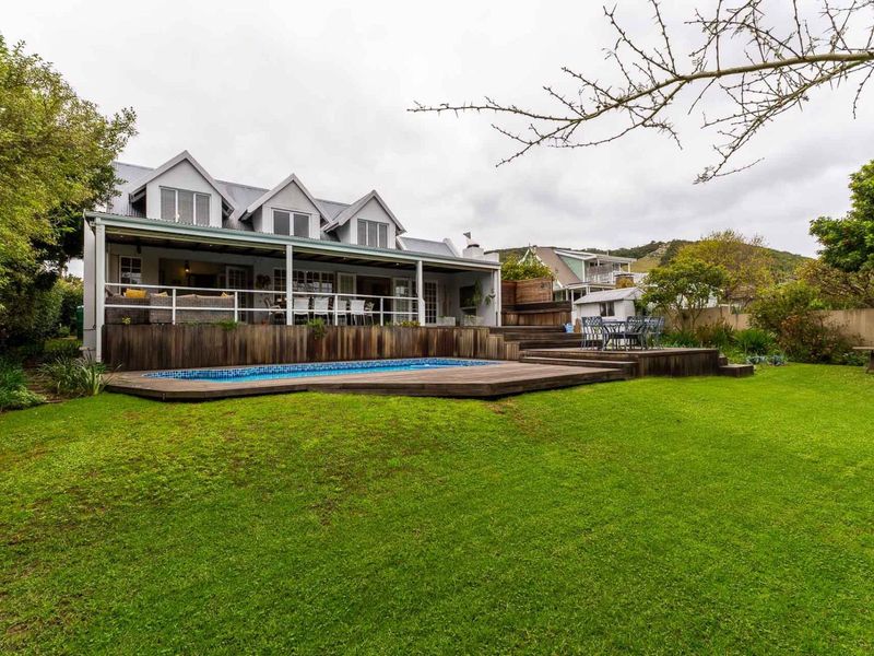 Rear view of the property featuring a swimming pool, extensive timber decking, a covered patio area, and a well-maintained garden.