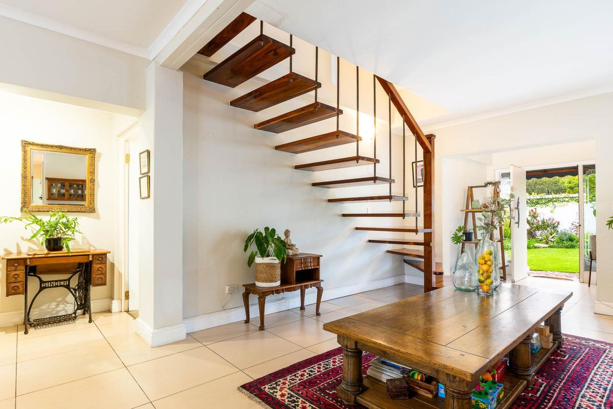 A bright living area featuring a modern floating wooden staircase, neutral tiled flooring, and direct access to the rear garden.