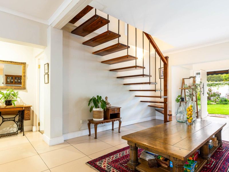A bright living area featuring a modern floating wooden staircase, neutral tiled flooring, and direct access to the rear garden.