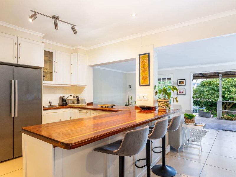 A bright, modern kitchen featuring white cabinetry, a warm timber breakfast bar, and direct access to an outdoor patio area.