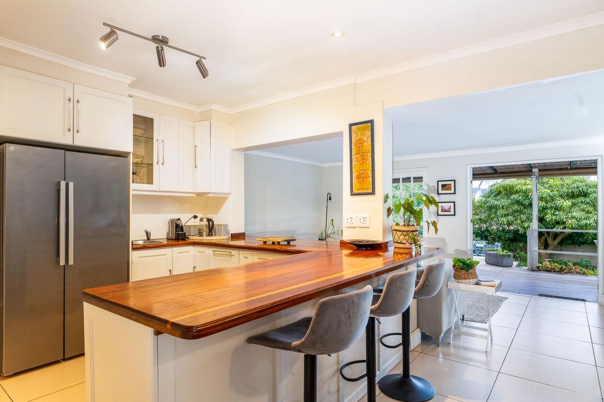 A bright, modern kitchen featuring white cabinetry, a warm timber breakfast bar, and direct access to an outdoor patio area.