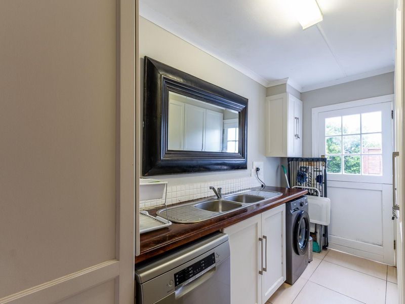 A functional laundry area featuring a double stainless steel sink, timber countertop, built-in cabinetry, and direct access to the exterior.