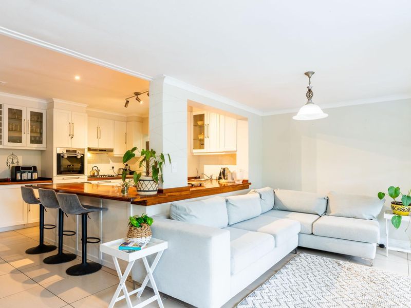 Open-plan living and kitchen area featuring a wooden breakfast bar, white cabinetry, built-in appliances, and tiled flooring throughout.