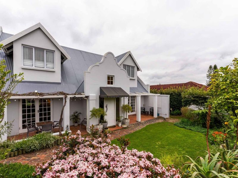 A charming rear exterior view featuring a gabled roof, brick paved patio, and a well-maintained landscaped garden.