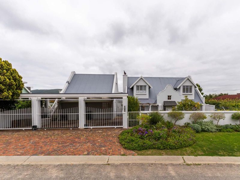 Front view of a charming house featuring a gabled roof, brick driveway, and a secure gated carport with a landscaped front garden.